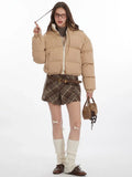 Woman adjusting her hair while wearing a beige cropped puffer jacket and glasses.