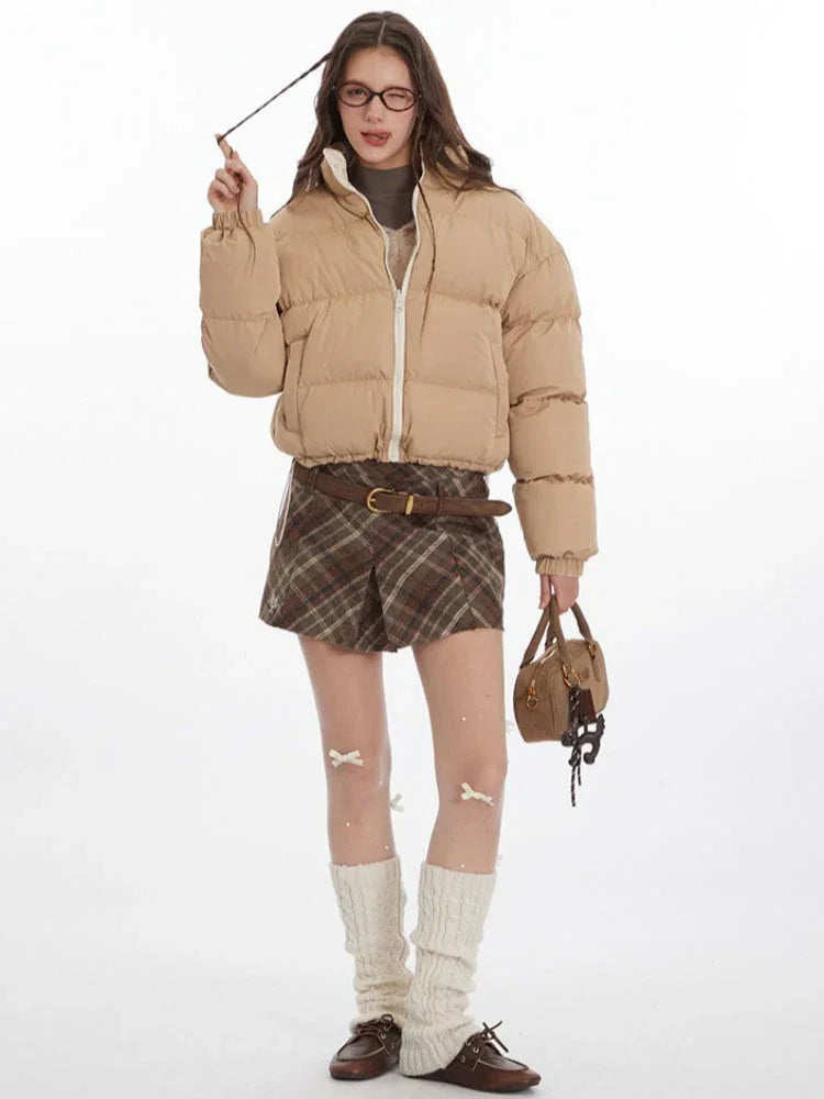 Woman adjusting her hair while wearing a beige cropped puffer jacket and glasses.