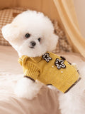 Side view of a white dog wearing a yellow knitted sweater with floral and bear appliques.