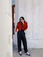 Woman wearing a red faux fur cropped jacket, black pants, and sneakers, standing and talking on the phone.