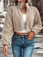Woman wearing a tan fuzzy fleece cropped bomber jacket with a stand collar and full zip closure.