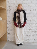 Full body shot of a model styled in a cream and black raglan sleeve sweater, argyle scarf, and white trousers.