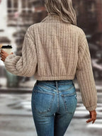 Back view of a woman in a tan fuzzy fleece cropped bomber jacket with ribbed texture.