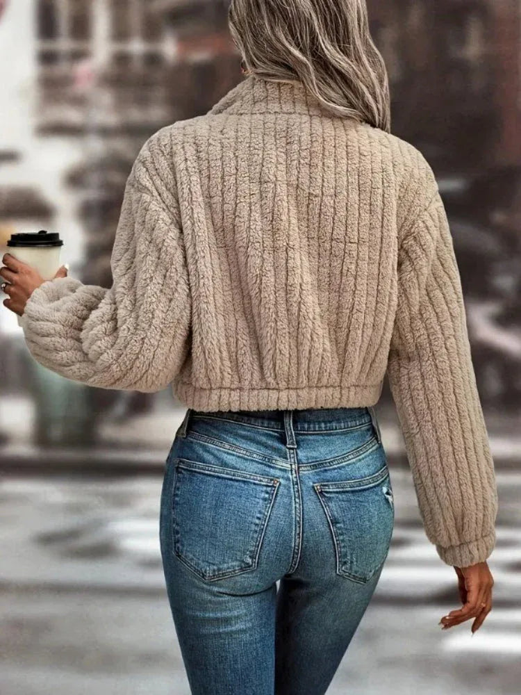 Back view of a woman in a tan fuzzy fleece cropped bomber jacket with ribbed texture.