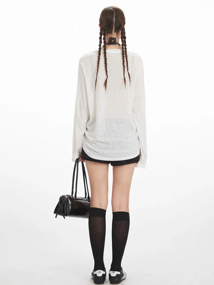 Woman wearing a white long-sleeve sheer knit t-shirt with a black dog graphic print and text, paired with black shorts and black knee-high socks.