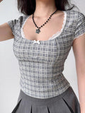Close-up of a woman wearing a grey plaid short sleeve top with a square neckline and white lace trim.