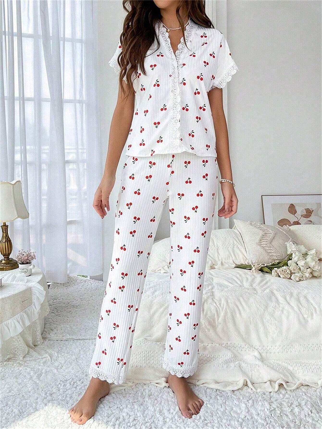 Woman wearing a white short-sleeve pajama top with a cherry print and lace trim, paired with white ribbed pajama pants featuring a cherry print and lace cuffs, standing in a bedroom. Main image