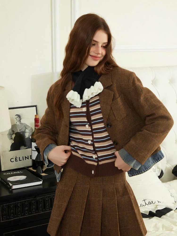 Woman wearing a brown plaid textured jacket, striped knit top, and brown pleated skirt.