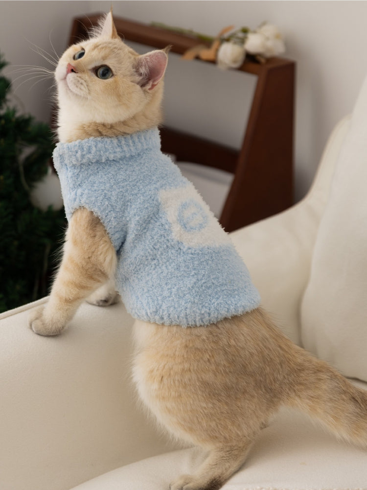 A cat in a light blue fluffy knit pet vest with a mock neck, looking upwards.
