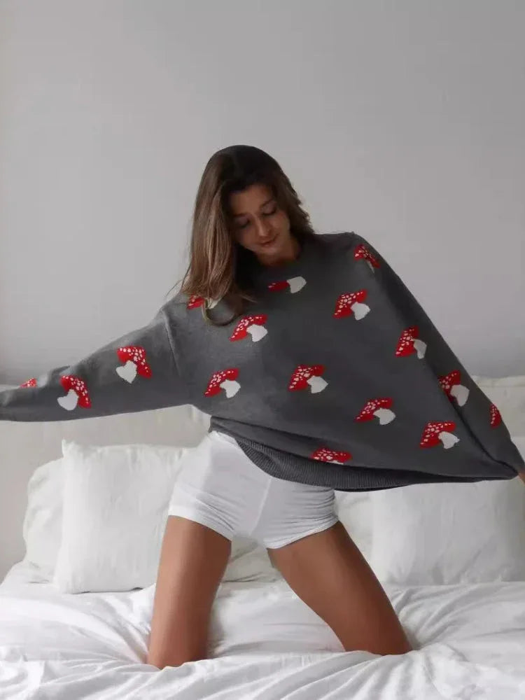 Woman wearing a grey knit sweater with a red and white mushroom print, arms outstretched.
