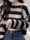 Close-up of a woman's torso wearing a grey and black striped cropped knit sweater with cut-out shoulders.