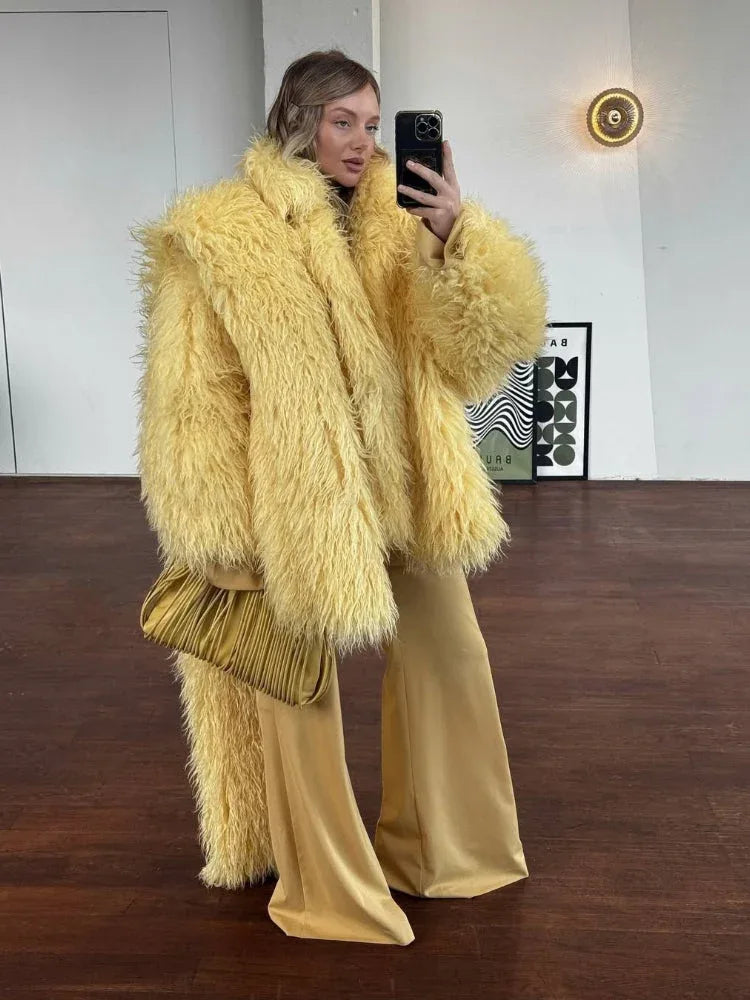 Woman wearing a yellow shaggy faux fur coat with wide-leg yellow pants and a gold clutch.