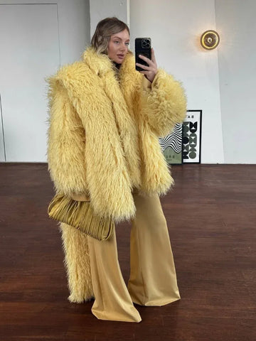 Woman wearing a yellow shaggy faux fur coat with wide-leg yellow pants and a gold clutch.