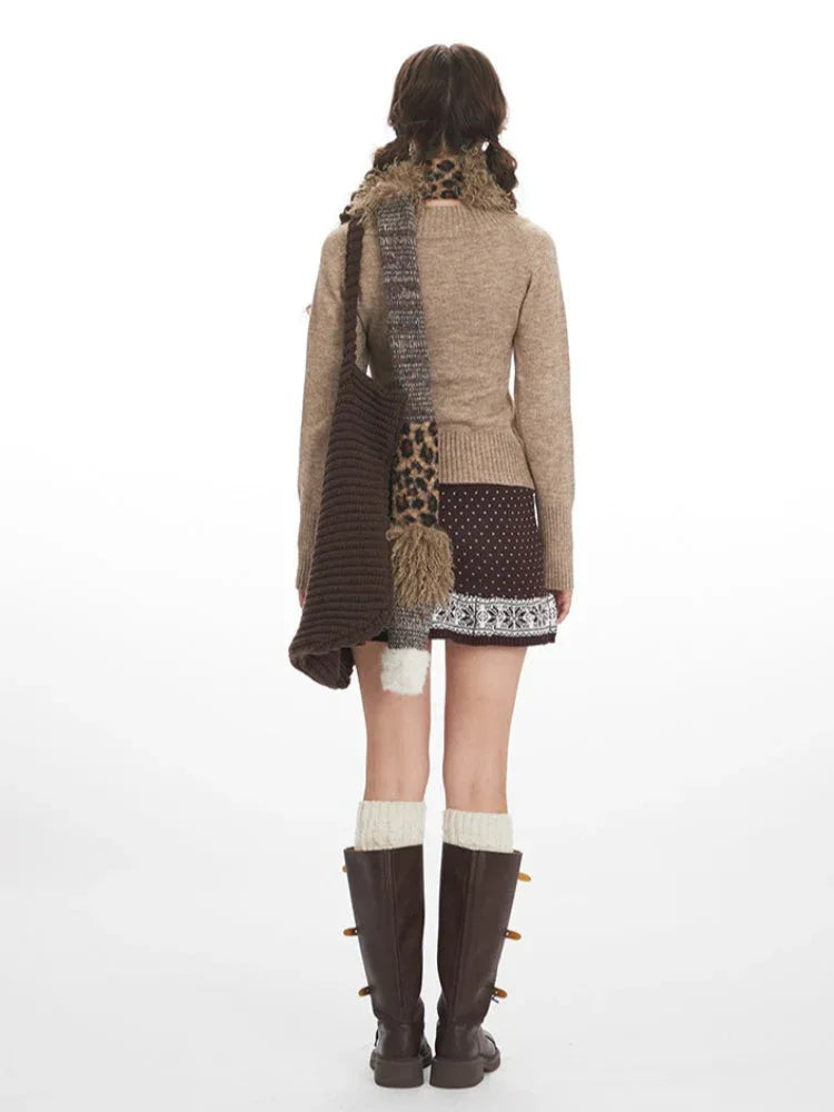 Back view of a woman in a beige V-neck knit sweater and brown patterned skirt.