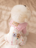 Back view of a white dog in a pink and striped pet jumpsuit with a bear applique and paw print label.