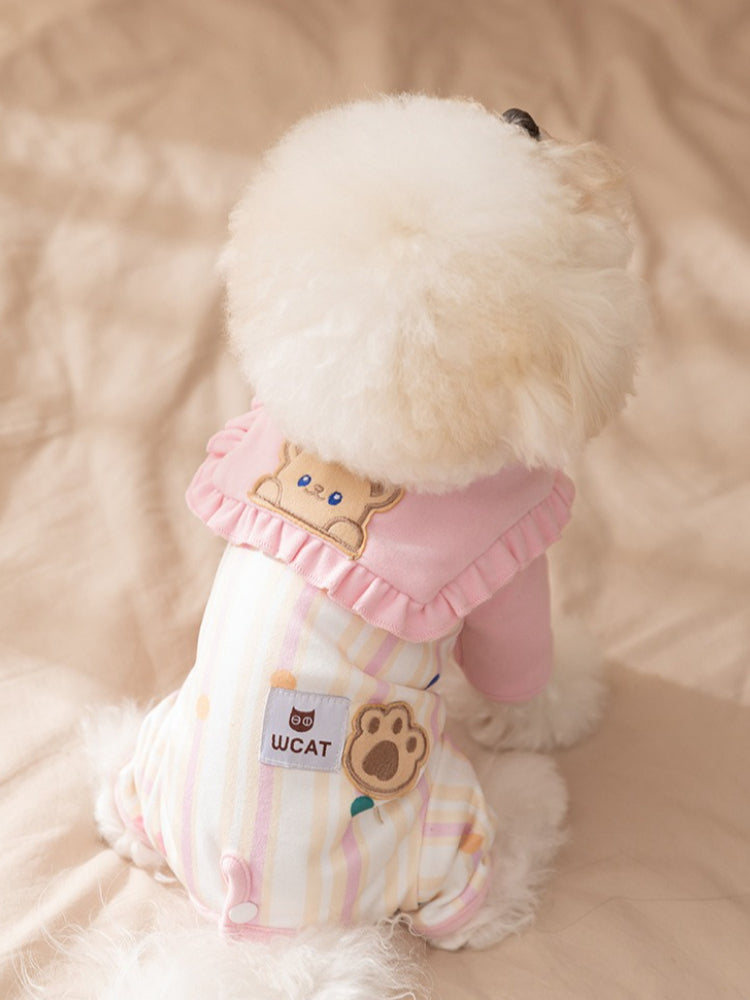 Back view of a white dog in a pink and striped pet jumpsuit with a bear applique and paw print label.