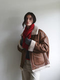 Woman adjusting a red knit scarf with grey gloves and a brown aviator jacket