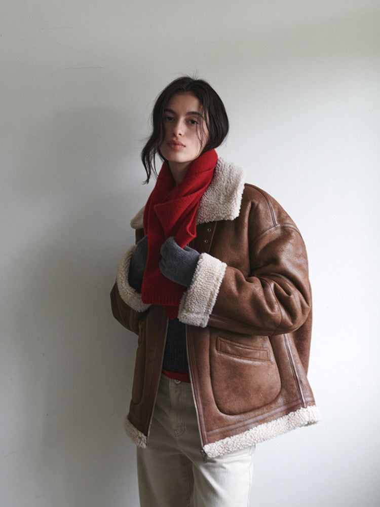 Woman adjusting a red knit scarf with grey gloves and a brown aviator jacket