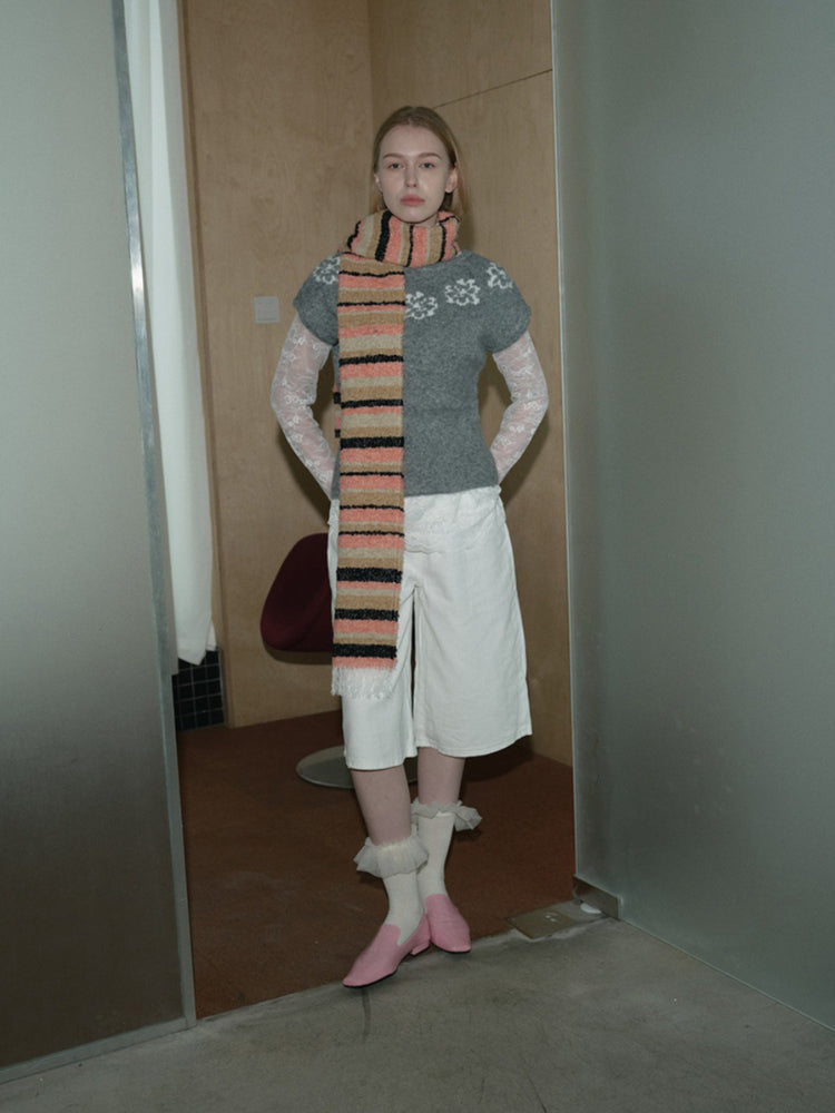 Woman wearing a grey short-sleeve sweater, white culottes, lace sleeves, a multi-colored striped scarf, and pink shoes.
