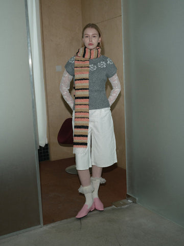 Woman wearing a grey short-sleeve sweater, white culottes, lace sleeves, a multi-colored striped scarf, and pink shoes.
