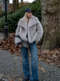 woman wearing a light grey faux fur jacket with a wide collar and black baseball cap