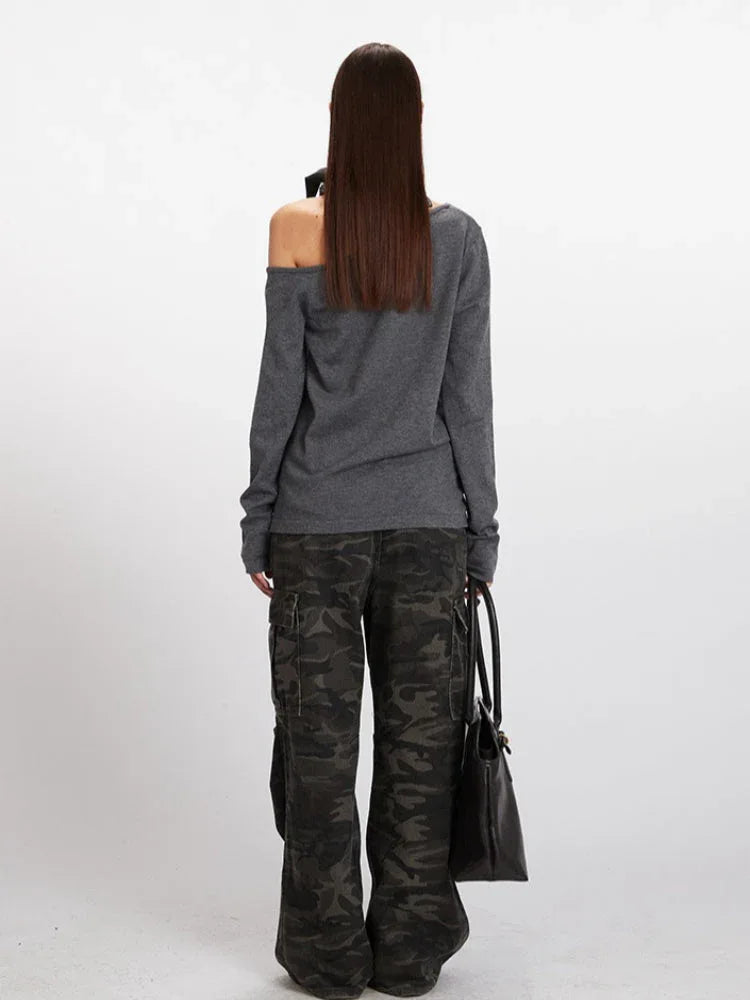 Back view of a woman in a grey knit cardigan with an asymmetrical neckline and long sleeves, holding a black handbag.