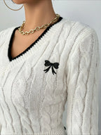 Close-up of the embroidered bow detail on a white cable knit V-neck sweater with black trim.