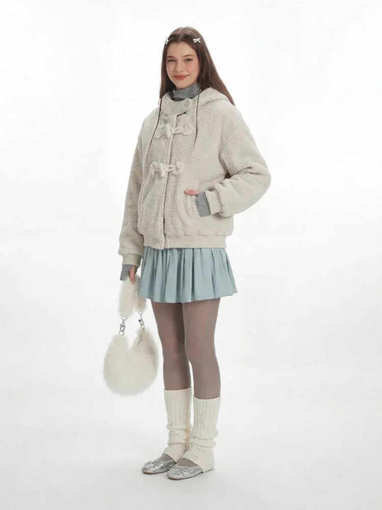 Full body shot of a woman in a cream fuzzy hooded jacket and a light blue pleated skirt.