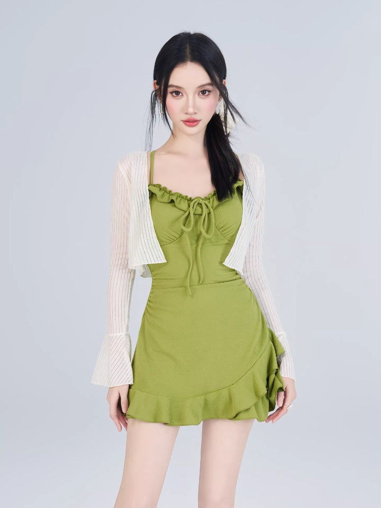 Woman wearing a green textured knit mini dress with ruffled trim and tie-front detail, paired with a white open-knit cardigan with flared sleeves.