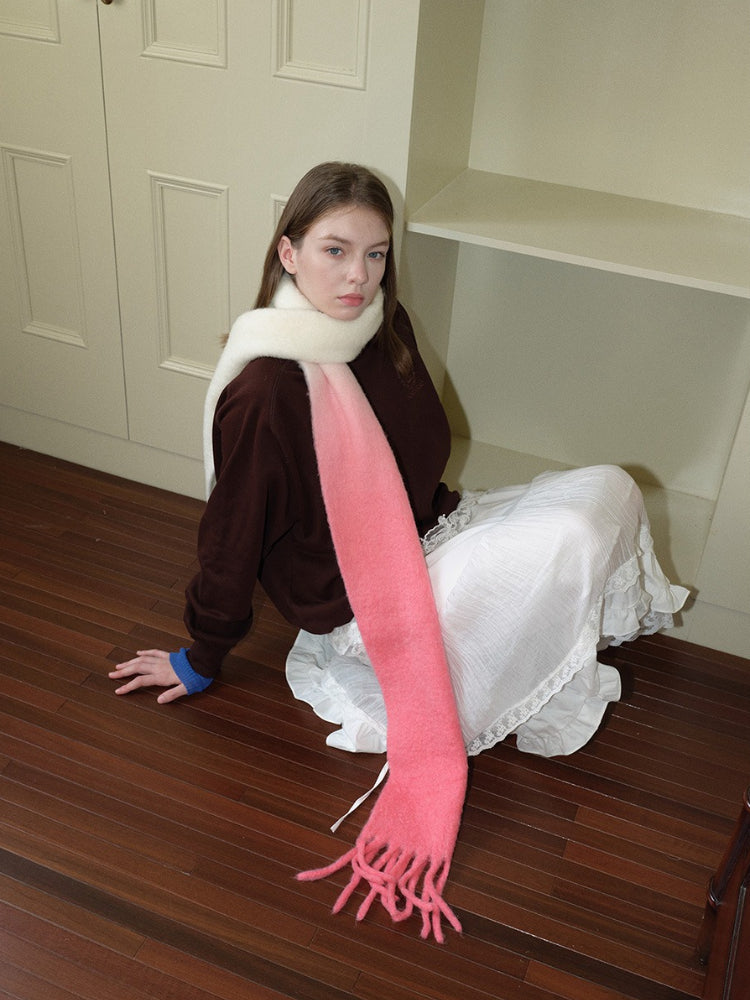 Model wearing a long, fuzzy knit scarf with a cream to pink ombre gradient and fringe trim.