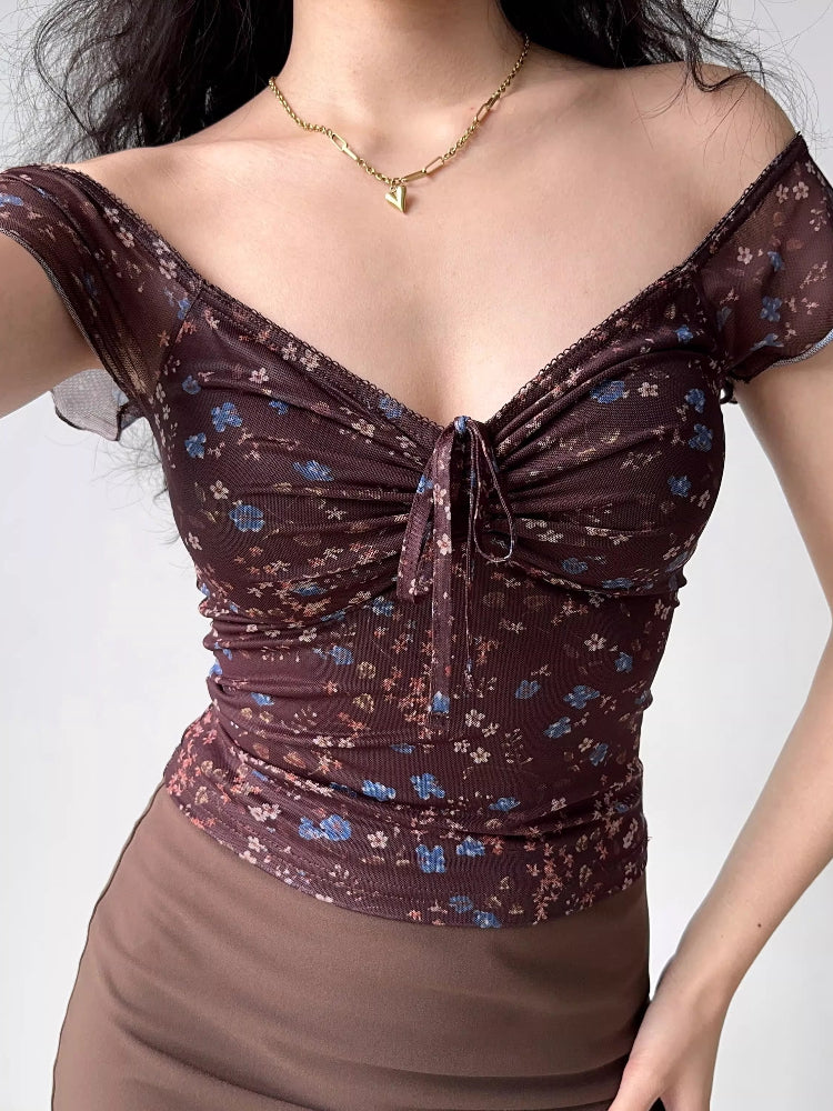 Woman wearing a brown floral print mesh top with short cap sleeves and a tie front detail.