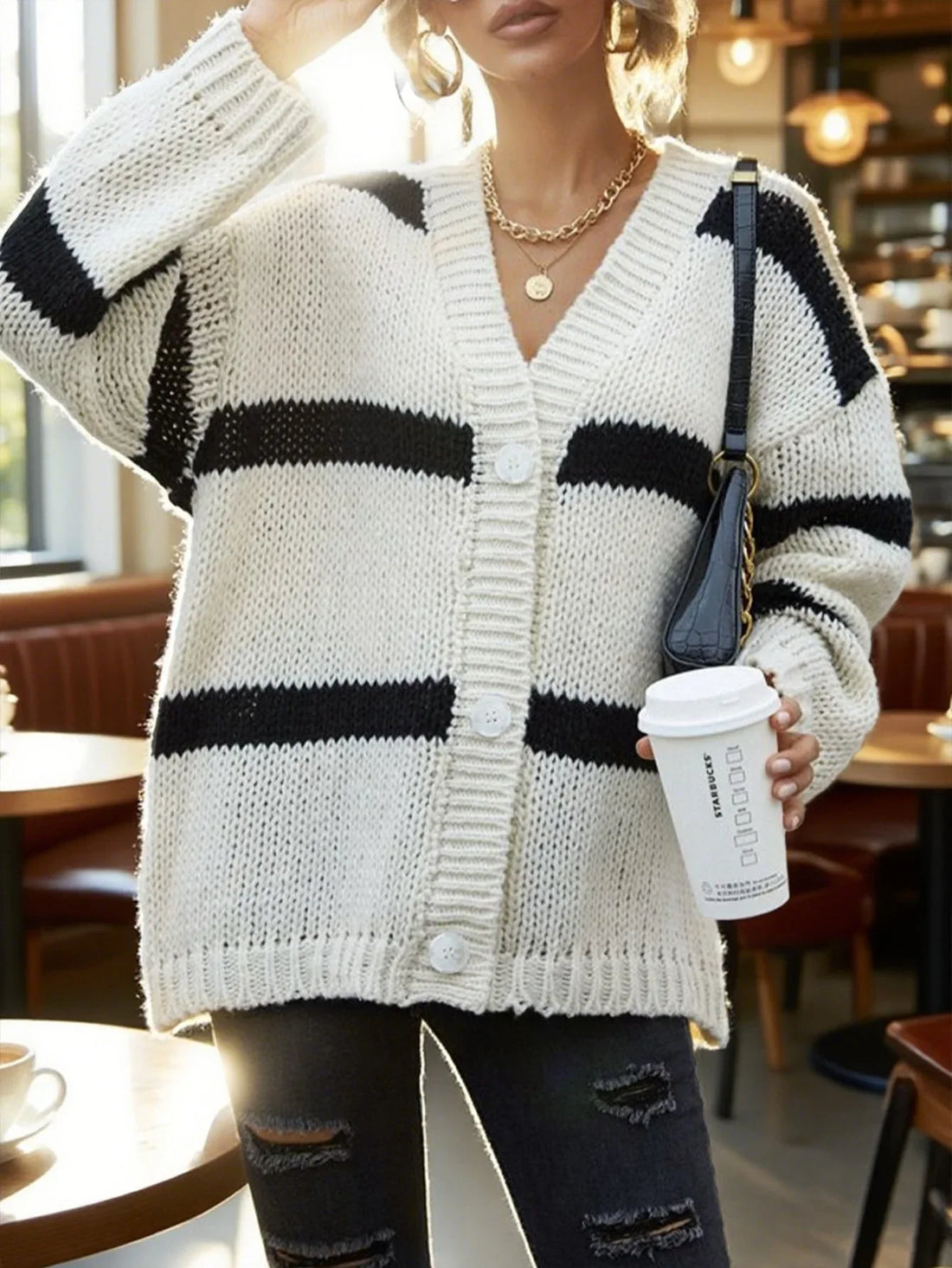 Woman wearing a white and black striped oversized knit cardigan with a white tank top and distressed black jeans.
