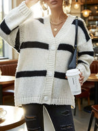 Front view of a woman in a white and black striped chunky knit cardigan, showcasing the button closure and V-neckline.