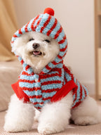 Dog wearing a blue and red striped hooded dog coat with a pom-pom on the hood.