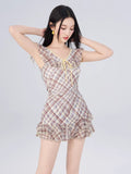 Woman posing in a plaid print dress with ruffled details and tie front.
