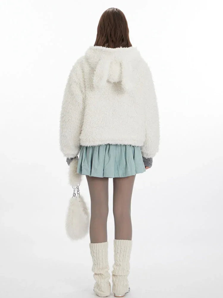 Back view of a woman wearing a white fuzzy fleece hooded jacket with bunny ears, a grey turtleneck, a light blue pleated skirt, grey tights, and white leg warmers.