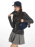 Close-up of a model adjusting her turtleneck sweater, showcasing the striped pattern and the pleated skirt.