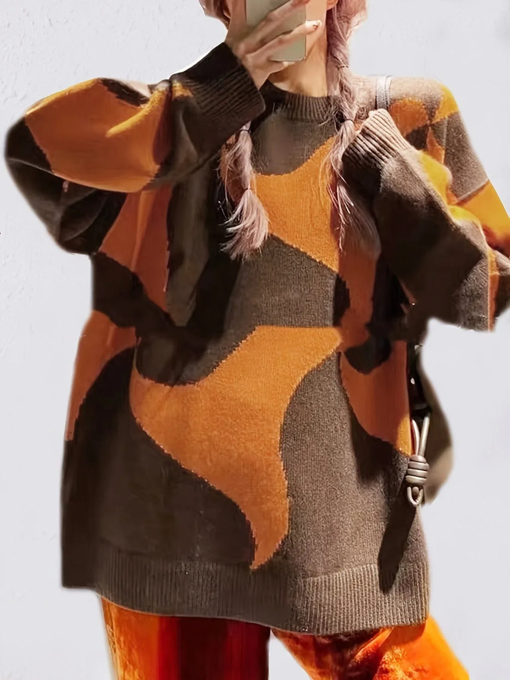 Close-up of a woman wearing a brown and orange abstract patterned knit sweater with pink braided hair.