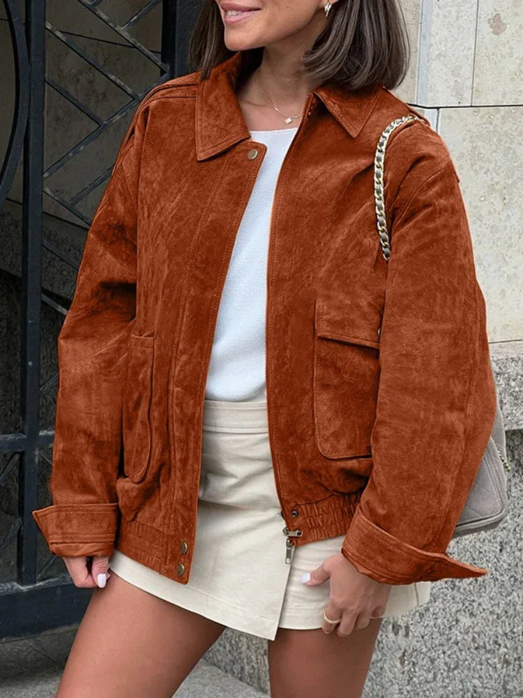 Woman wearing a brown suede-like bomber jacket with a white t-shirt and a beige skirt.