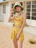 Model wearing a yellow plaid halter neck bikini top and skirted bottom, posing outdoors.