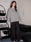 Model posing in a grey graphic print sweatshirt and dark wide-leg pants.