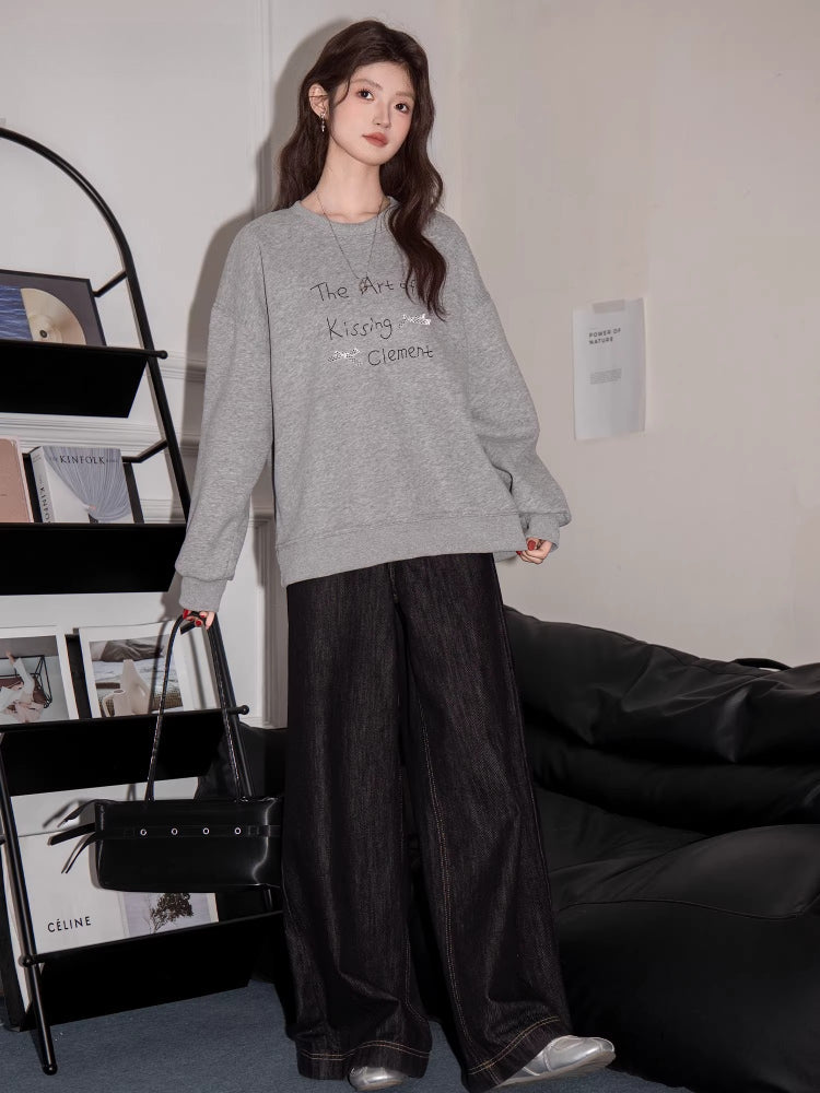 Model posing in a grey graphic print sweatshirt and dark wide-leg pants.