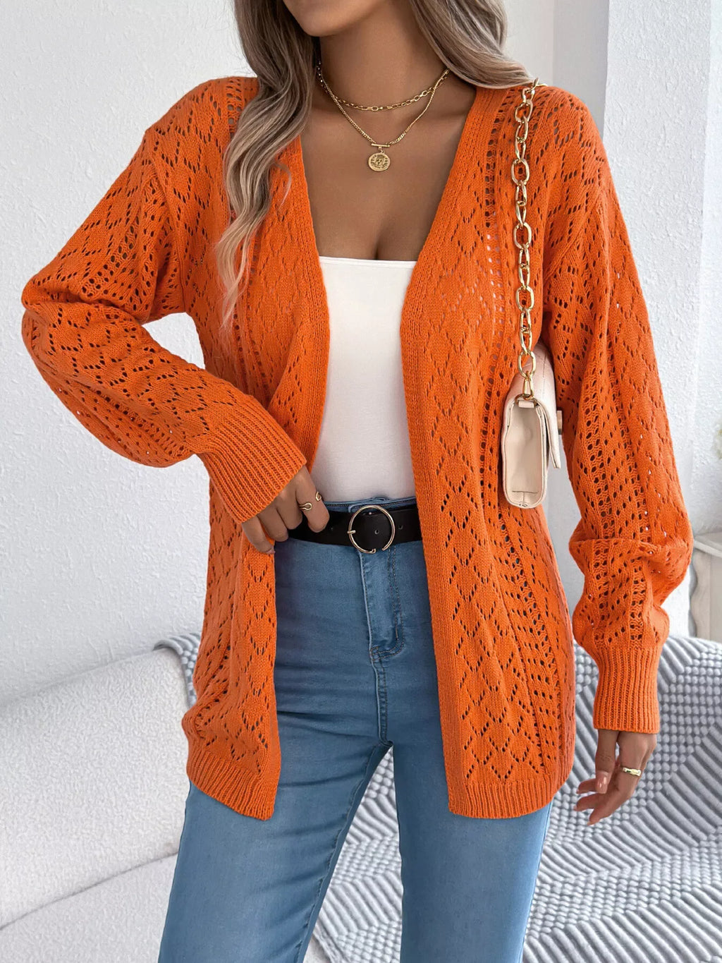 Close-up of a woman wearing an orange open-knit cardigan with a white tank top and blue jeans.