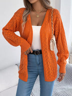Close-up of a woman wearing an orange open-knit cardigan with a white tank top and blue jeans.