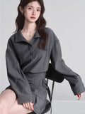 Woman wearing a grey long-sleeve collared shirt and a grey asymmetrical skirt