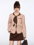 Woman wearing a light pink knit cardigan with dark brown trim and a decorative scarf