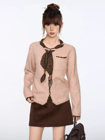 Woman wearing a light pink knit cardigan with dark brown trim and a decorative scarf