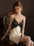 Woman wearing a cream-colored satin slip dress with black lace trim, sitting on a chair.