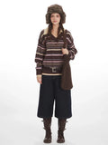Woman wearing a brown striped knit sweater with a v-neck and collar detail, dark wash wide-leg cropped jeans, brown leather boots, a brown belt, and a brown faux fur hat with ear flaps.