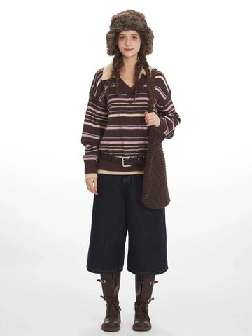 Woman wearing a brown striped knit sweater with a v-neck and collar detail, dark wash wide-leg cropped jeans, brown leather boots, a brown belt, and a brown faux fur hat with ear flaps.